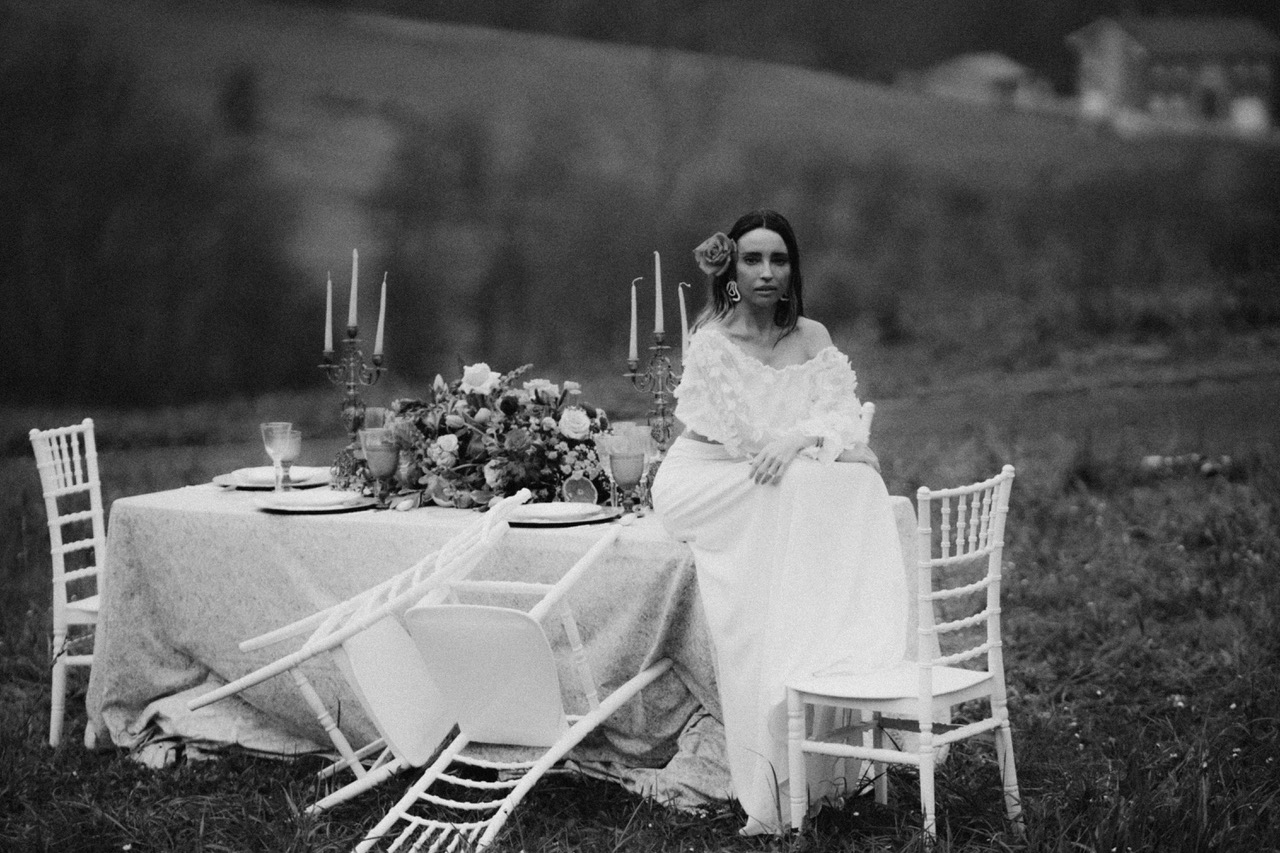 Una mujer vestida de novia sentada en una mesa de celebración en Blanco y negro mirando fijamente