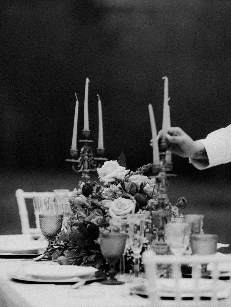 En la imagen se ve una mesa decorada con flores y candelabros y una mano de mujer