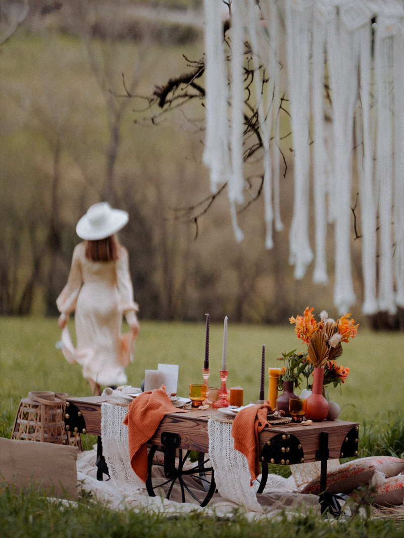 Se muestra una mesa decorada en el campo con una silueta de mujer alejandose