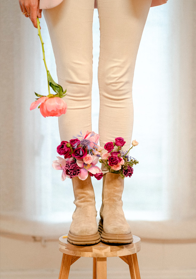 Se ven unos pies de mujer con unas botas de las cuales salen flores